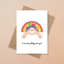 Load image into Gallery viewer, LGBTQ+ Valentine's card featuring two hands forming a heart with a rainbow arching overhead, and the message "I love being gay with you!"