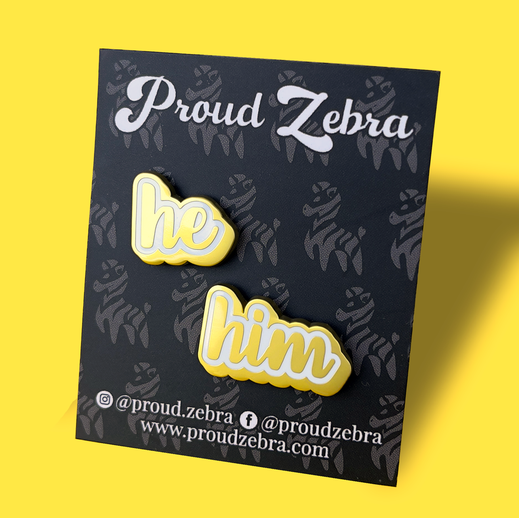 He/Him matte gold and white pronoun pins on black backing card by proud zebra