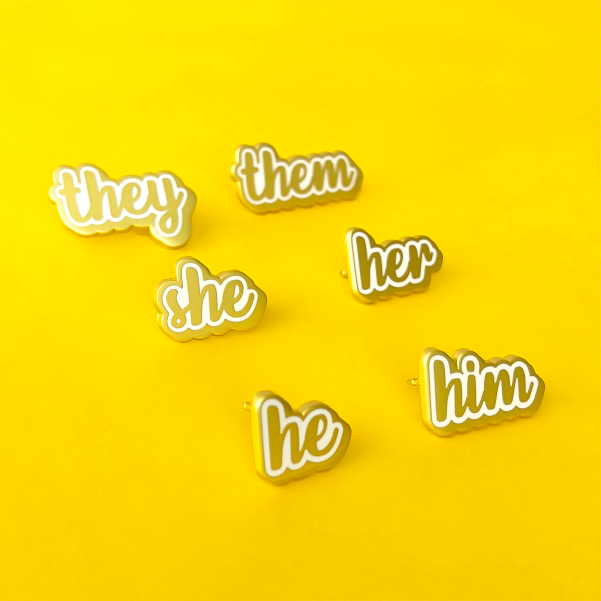 she/her, she/they, he/him, he/they, they/them matte gold and white enamel pronoun pins by proud zebra